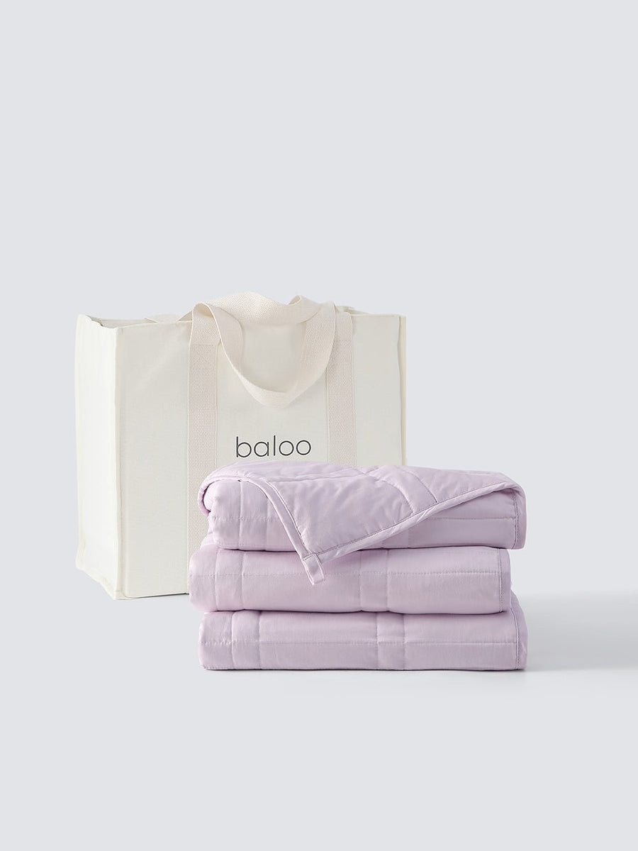 A folded weighted blanket in lavender color in front of a baloo tote bag on a white background [47867972059355, 47880476688603]