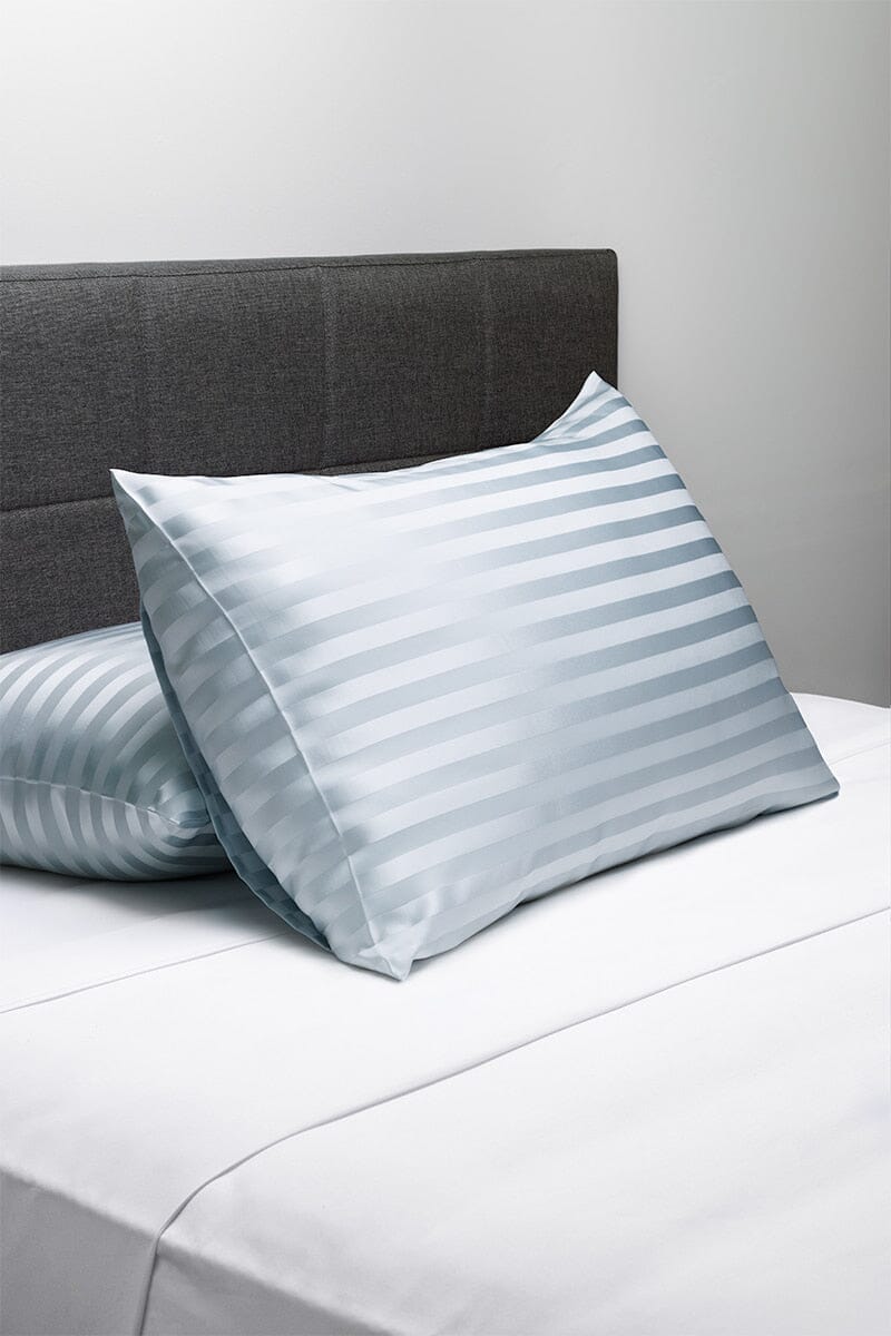Silver striped silk pillowcases on a white sheet with a dark gray headboard background.