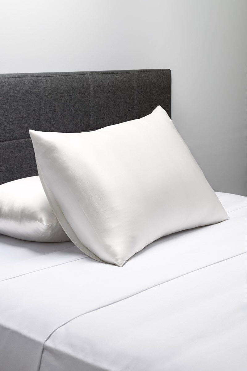 Smooth white silk pillowcases on a bed with a gray upholstered headboard.