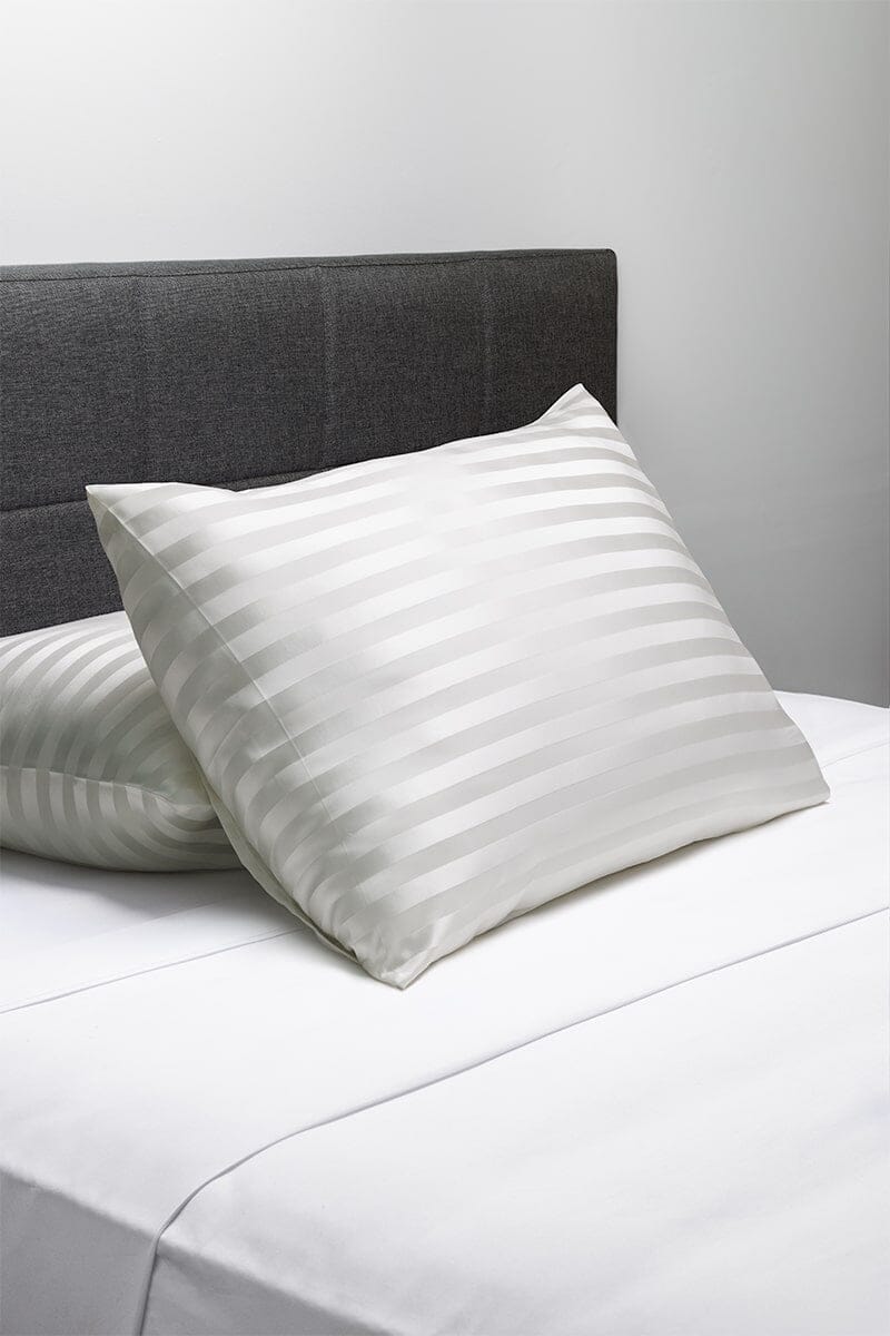 Silver silk pillowcase with subtle striped pattern on white bedding.