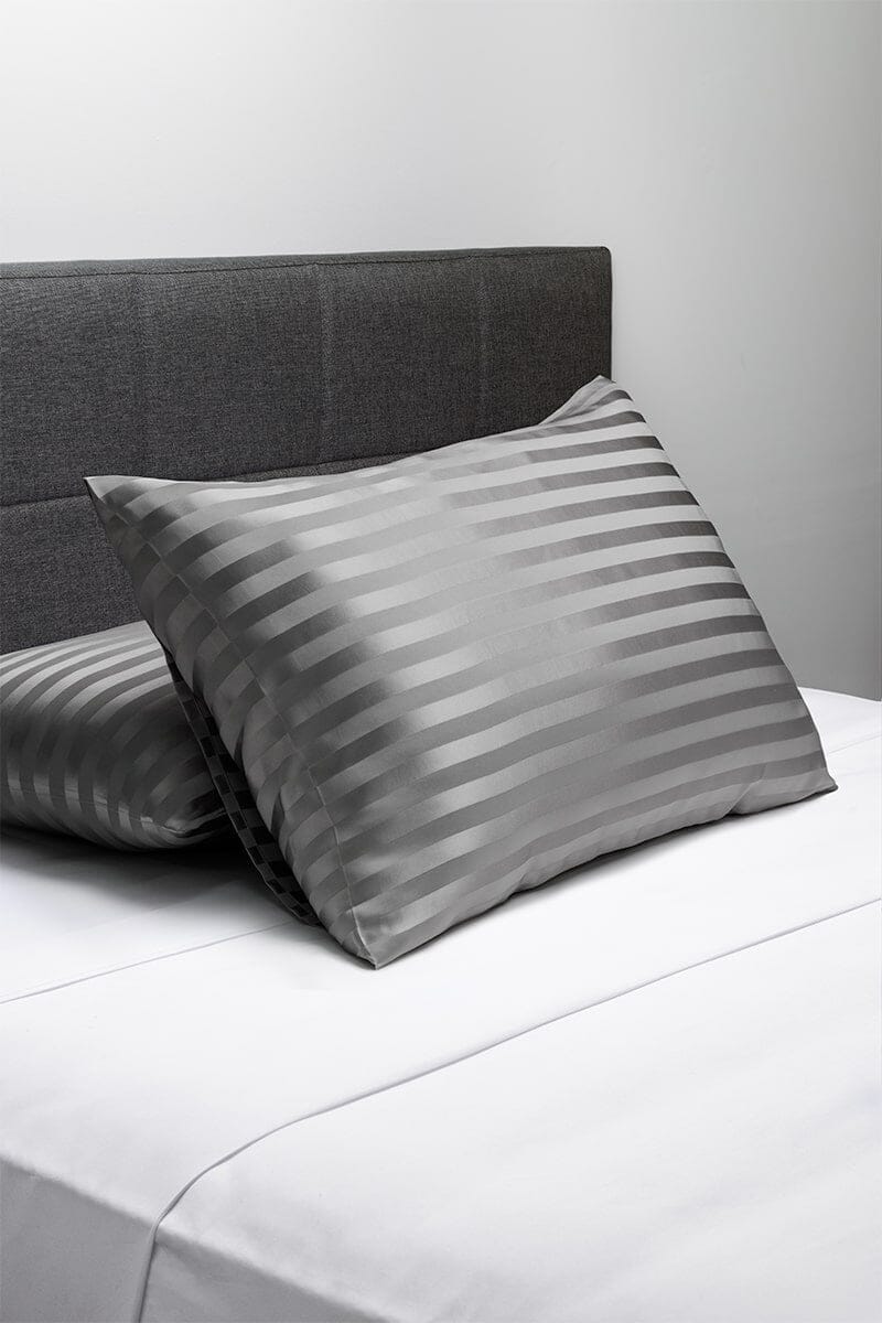 Silver striped silk pillowcases on white bedding with dark gray headboard.