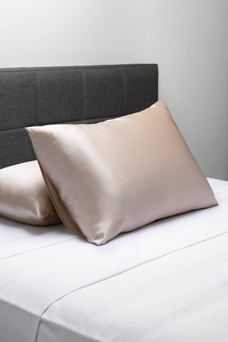 Silver silk pillowcase on white bed with grey upholstered headboard.